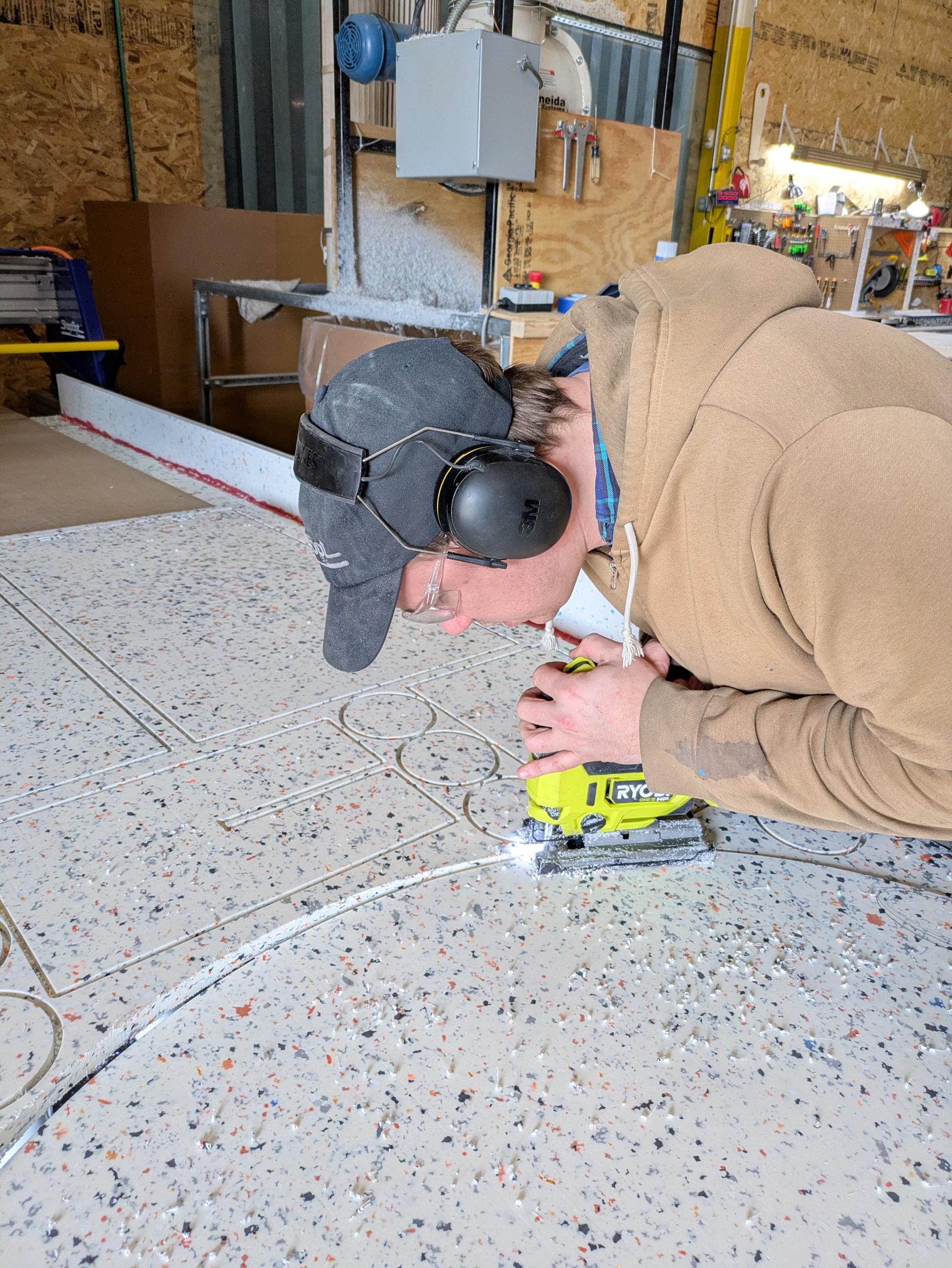 CNC-cut White Stone panel laid flat with circular and rectangular cutouts being released by hand-jigsaw.