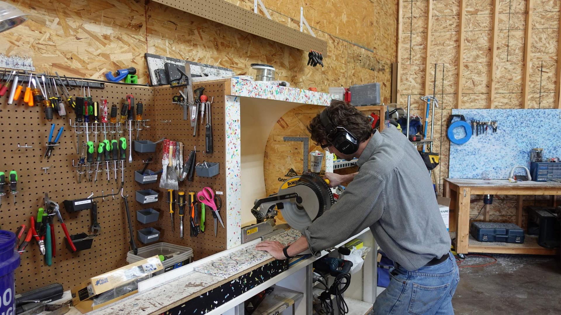 Marble Plastics fabricator in ear protection cutting a speckled recycled-plastic panel on a miter saw in the fabrication studio.