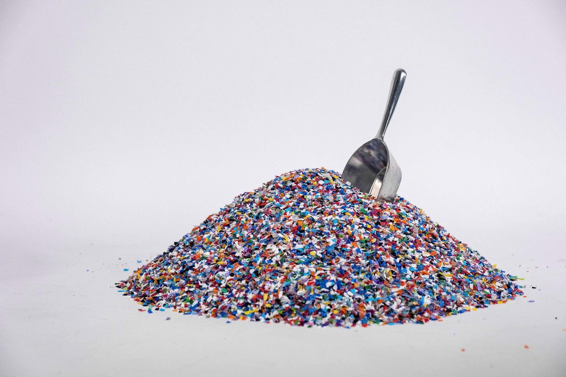 A pile of mixed post-consumer plastic flake with a metal scoop.