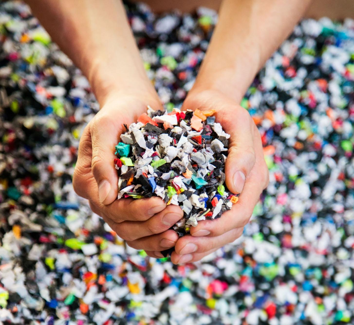 Hands holding a mix of recycled plastic flake — Nike Grind feedstock.